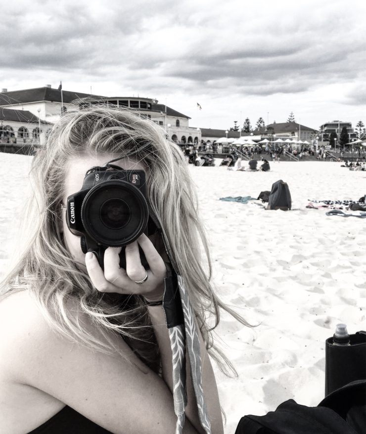 woman holding a camera sitting on a beach