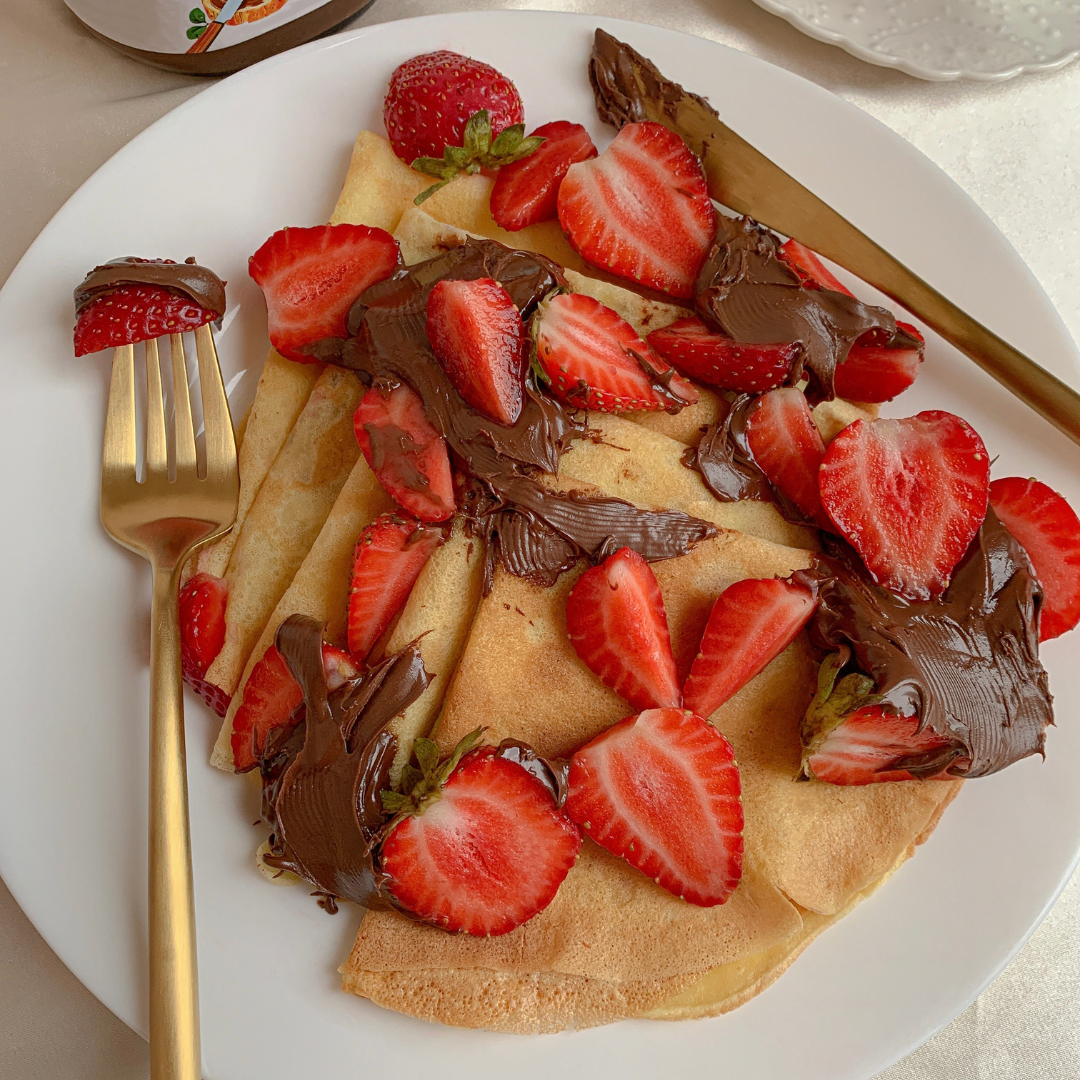 Crepes covered in chocolate and strawberries beside a gold colored fork.