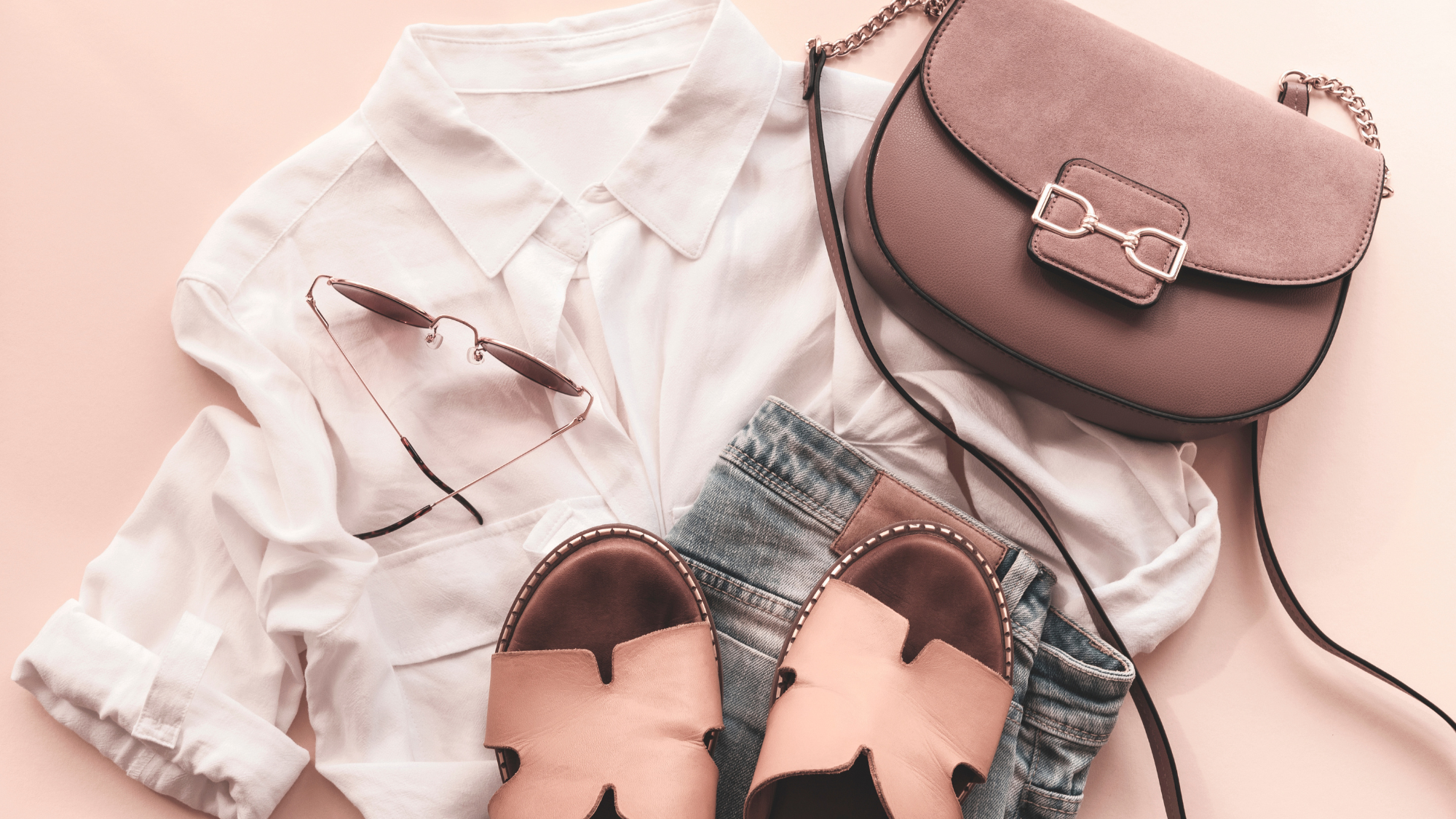 Women's button down shirt, jeans, sandals, handbag, and glasses arranged on the floor.