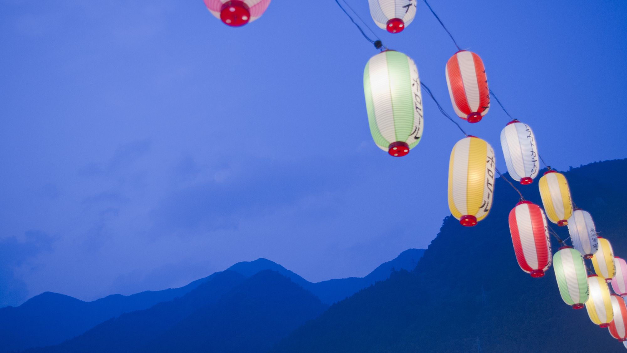Japanese lanterns in front of a mountain range at twilight.